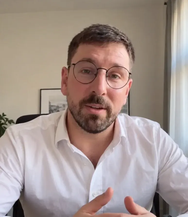 Ein Mann mit Brille und weißem Hemd spricht in einem Video-Gespräch in die Kamera