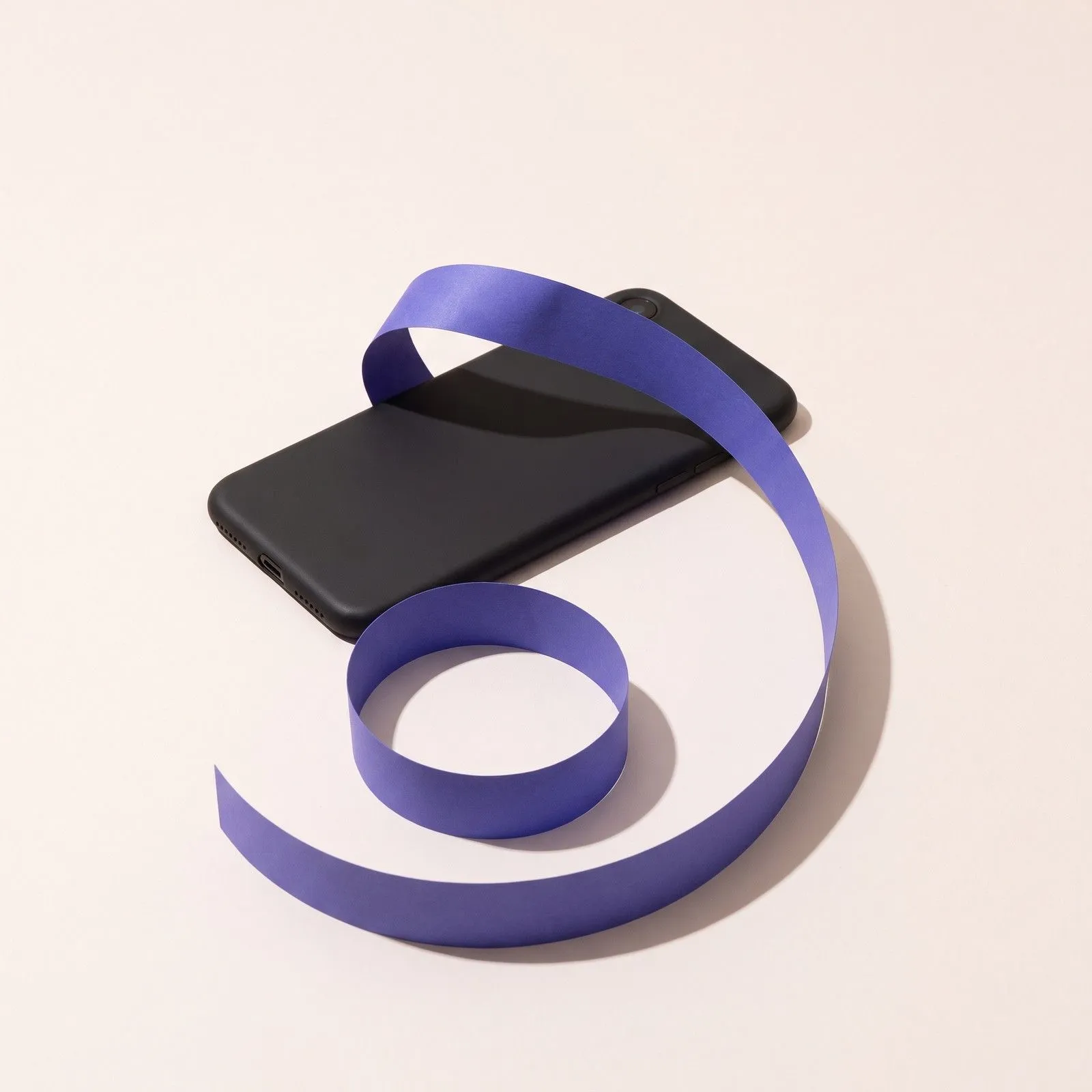 Ein Smartphone mit dunklem Display, aus dem sich ein langer violetter Papierstreifen zu einer Spirale rollt