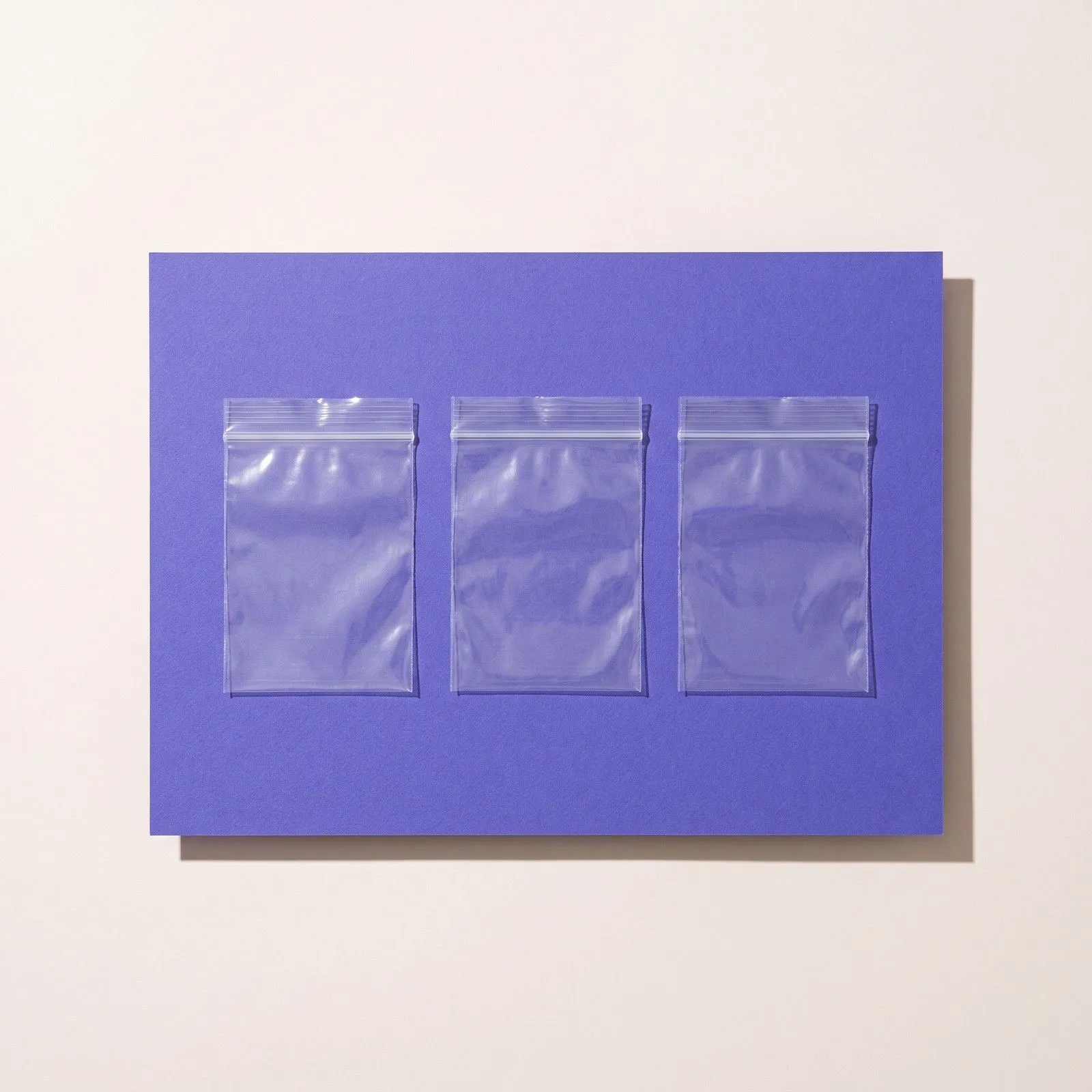 Drei leere durchsichtige Druckverschlussbeutel in einer Reihe auf violettem Papier
